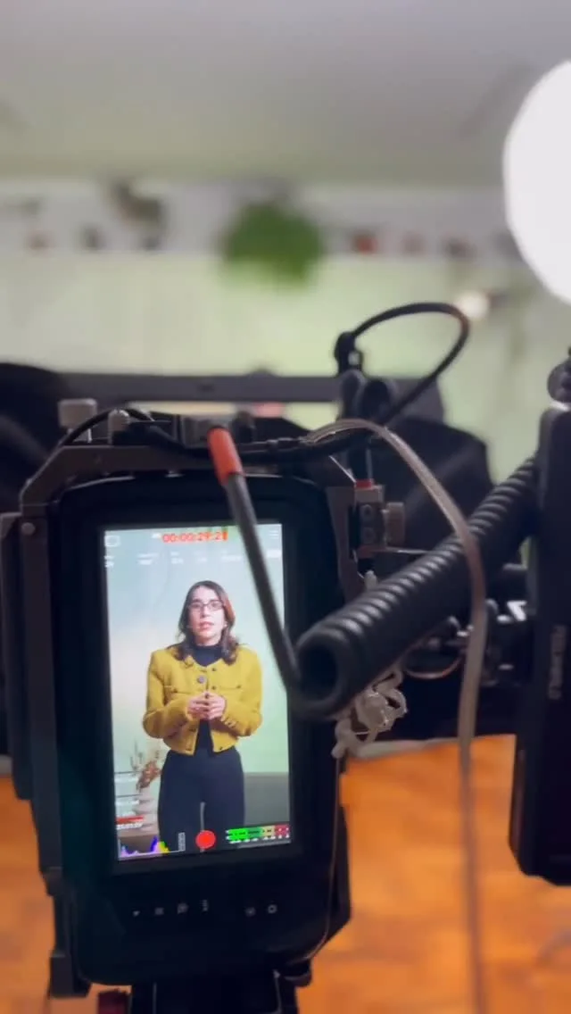 Câmera com microfone gravando uma apresentadora de casaco amarelo em uma locação